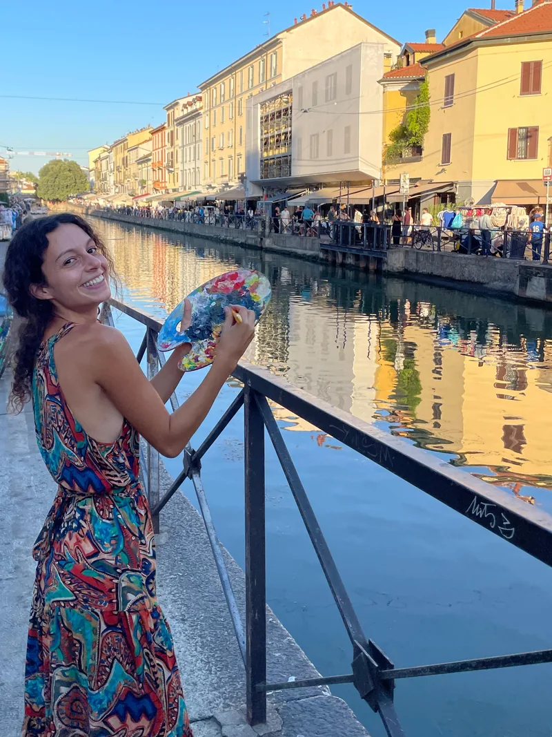 Sul Naviglio, a Milano, Giulia Dal Bon, pittrice formata all’Accademia di Brera, sorride con la tavolozza di colori in mano.