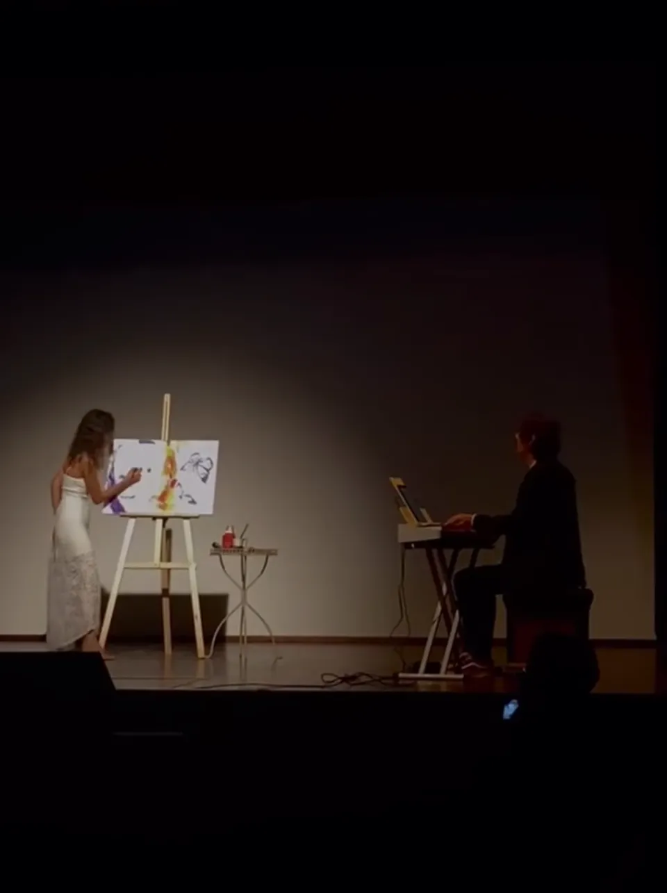 Su un palco di teatro, Giulia Dal Bon dipinge mentre Orlando suona la tastiera