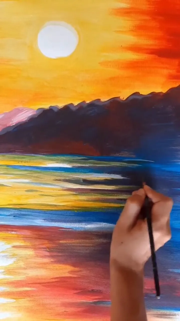 Giulia Dal Bon dipinge a pennello un paesaggio marino: il sole tramonta in un cielo arancione, sopra le montagne e il mare.