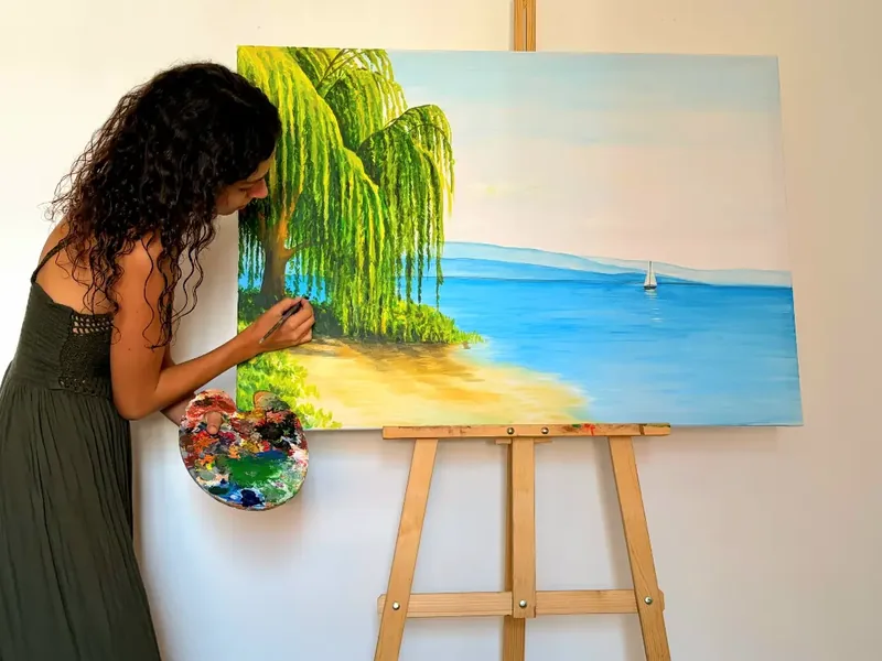 Penchée sur son chevalet, Giulia Dal Bon travaille au pinceau les verts du saule pleureur, sur une toile de 100 × 70 cm.