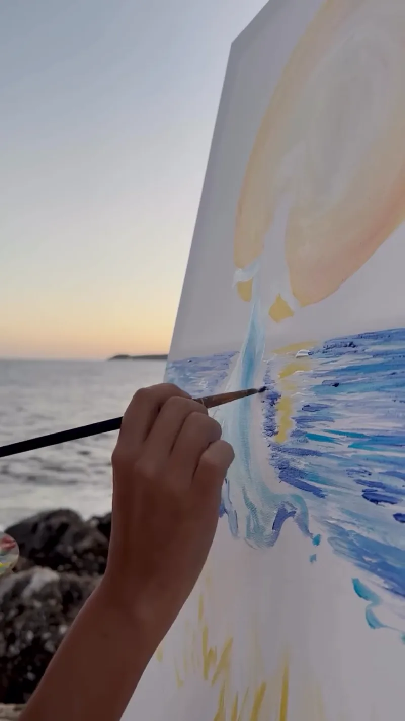 Au bord de l’eau, Giulia Dal Bon peint au pinceau le reflet du soleil qui scintille sur la mer.