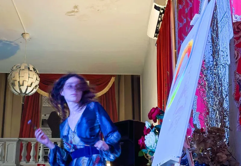 Pendant un live painting, Giulia Dal Bon danse avec le pinceau devant sa toile, dans une salle aux rideaux rouges.