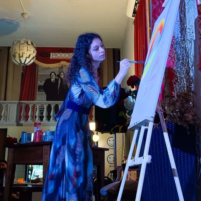 Dans une salle aux rideaux rouges, Giulia Dal Bon peint en direct les premières lignes de couleur sur une grande toile.