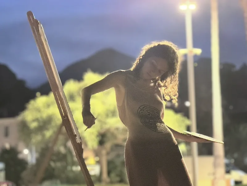 Live painting al aire libre, al anochecer: Giulia Dal Bon pinta a la luz de las farolas, con la paleta en la mano.
