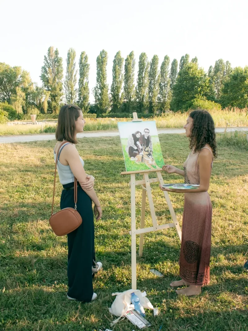 Giulia Dal Bon dipinge al cavalletto il ritratto di un’ospite, in un parco.