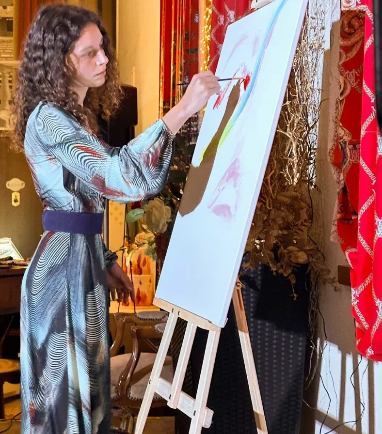 Live painting in a reception room: standing at the easel, Giulia Dal Bon paints a large canvas against red drapes.