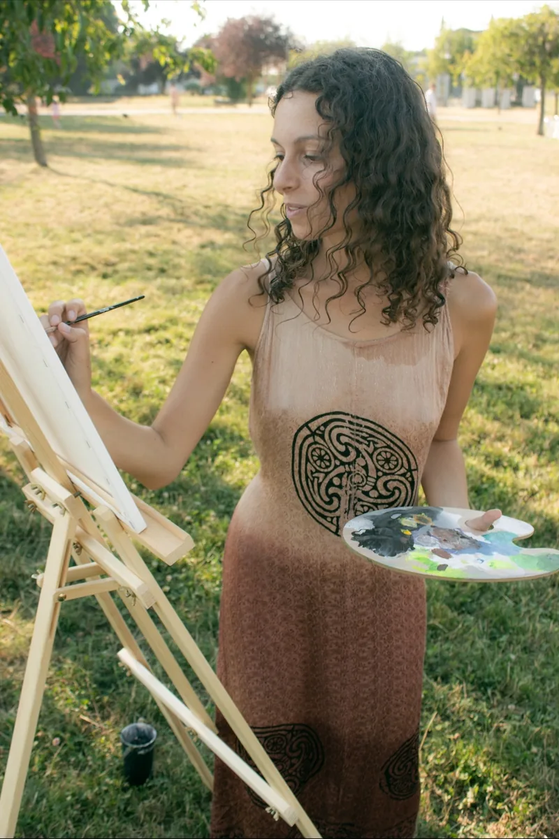 Live painting in un parco: Giulia Dal Bon dipinge al cavalletto, tavolozza in mano, nella luce dorata della sera.