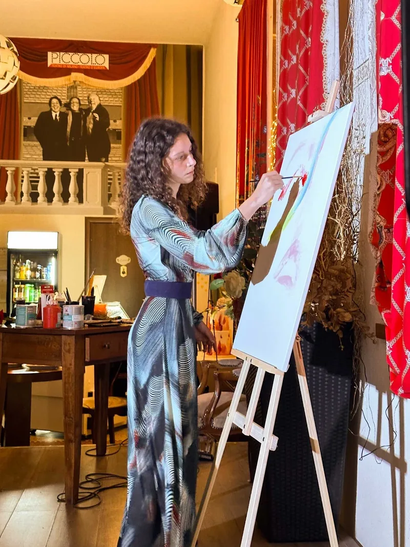 Example of live painting on Lake Como: in a reception room with red curtains, Giulia Dal Bon, in a blue dress, paints at her easel.
