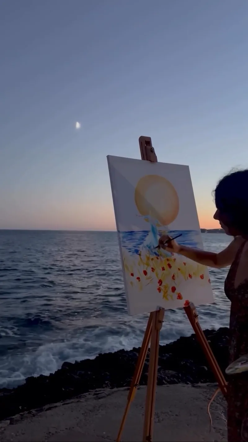Au bord de la mer, Giulia Dal Bon peint sur sa toile un grand soleil qui se couche sur les vagues.