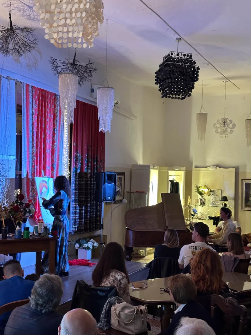 Spettacolo di pianoforte e pittura: sotto una luce blu, Giulia Dal Bon dipinge accanto al pianoforte a coda davanti al pubblico.