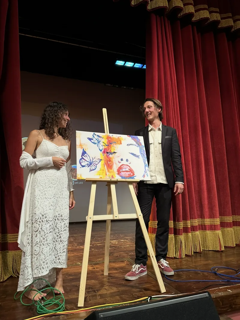 At the end of the piano and painting show, Giulia Dal Bon and Orlando stand beside the finished painting, before the red curtain.