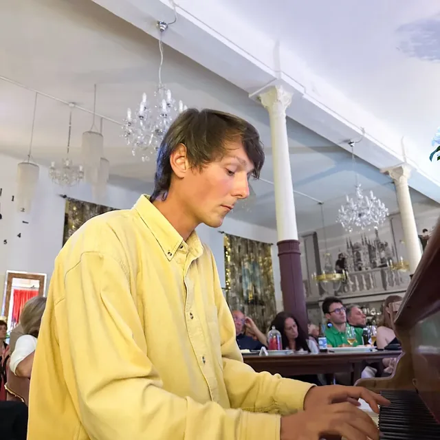 Pendant le spectacle d’Orlando & Giulia, Orlando joue du piano devant le public attablé, sous les lustres.