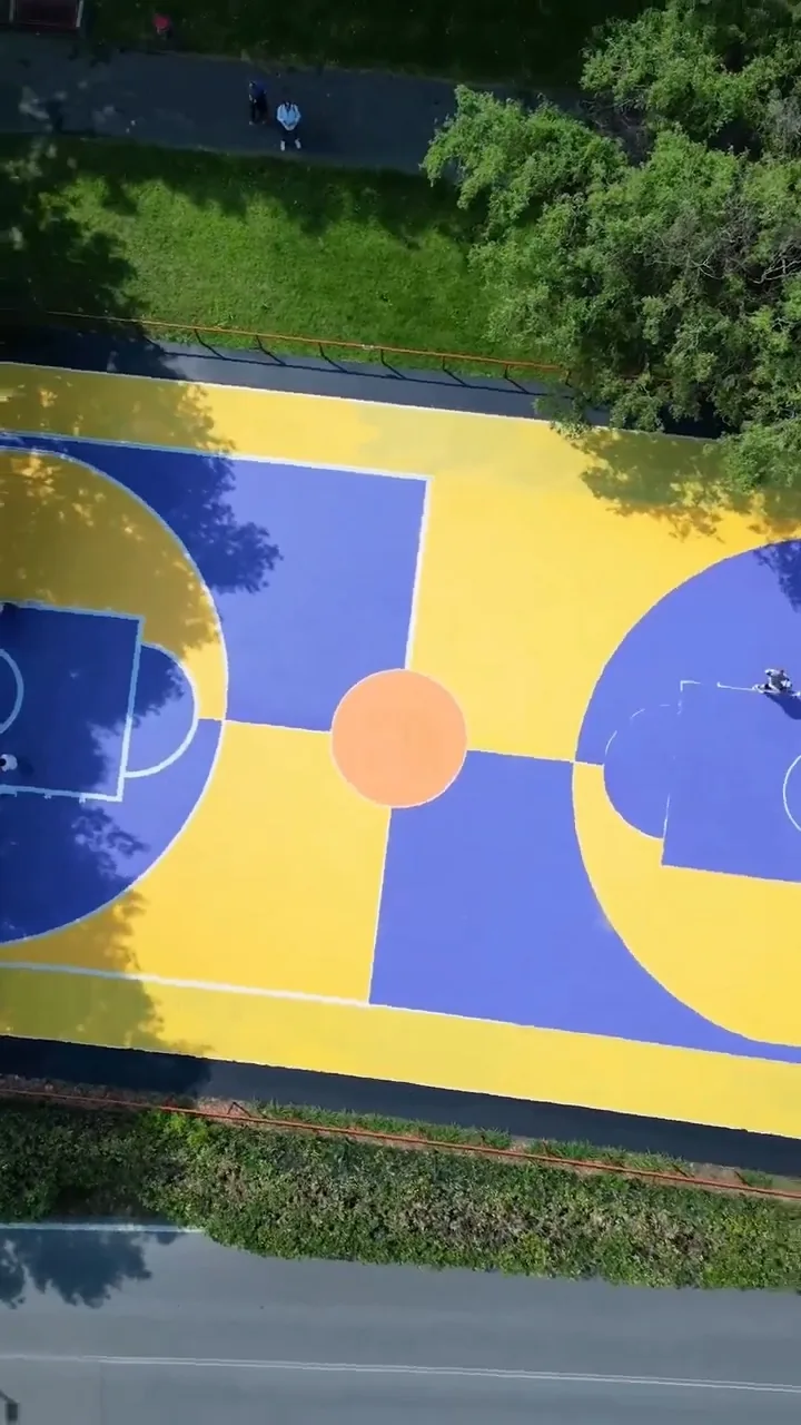 Giulia Dal Bon repainted a basketball court in yellow and blue with an orange centre circle, photographed here from above.