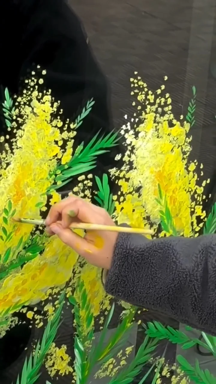 Giulia Dal Bon peint au pinceau des branches de mimosa, d’un jaune éclatant sur un fond sombre.