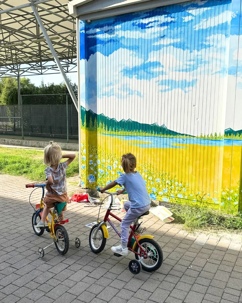 Ejemplo de mural en Gstaad: Giulia Dal Bon cubrió de flores una fachada, y dos niños en bicicleta la miran.