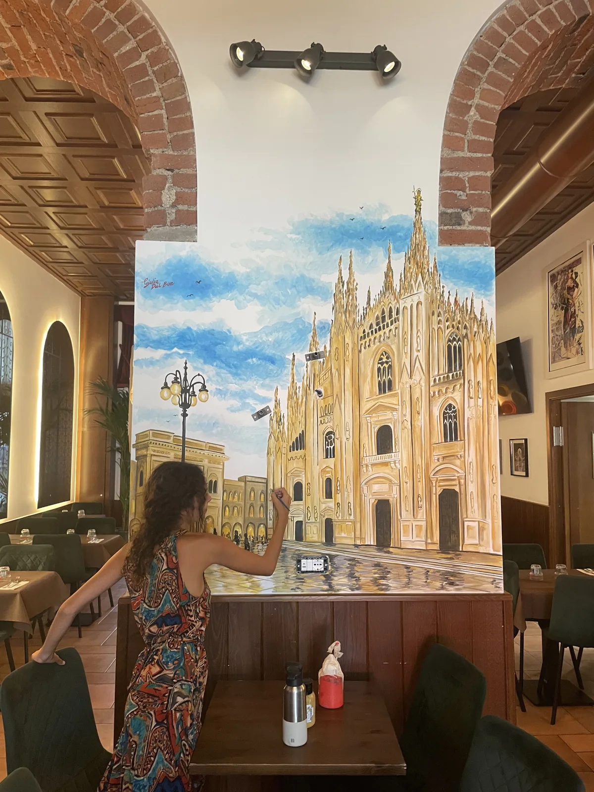 In un ristorante milanese con archi di mattoni, Giulia Dal Bon dipinge il selciato lucido ai piedi del Duomo del suo murale.