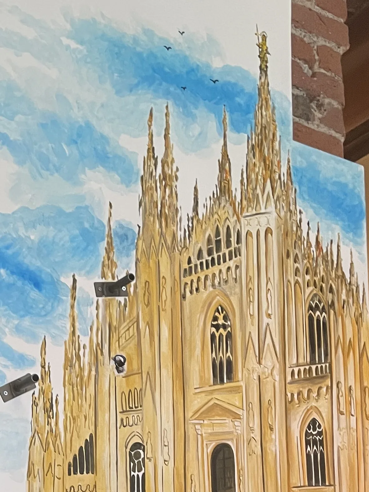 Da vicino, le guglie del Duomo e la Madonnina dorata dipinte a pennello da Giulia Dal Bon si stagliano sul cielo azzurro.