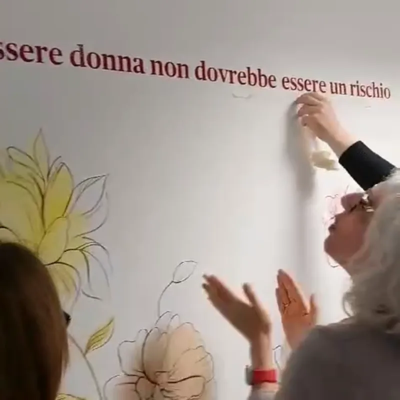 Esempio di murale con un messaggio: Giulia Dal Bon ha dipinto grandi fiori a linee sotto una frase in lettere rosse, e il pubblico applaude davanti al muro.