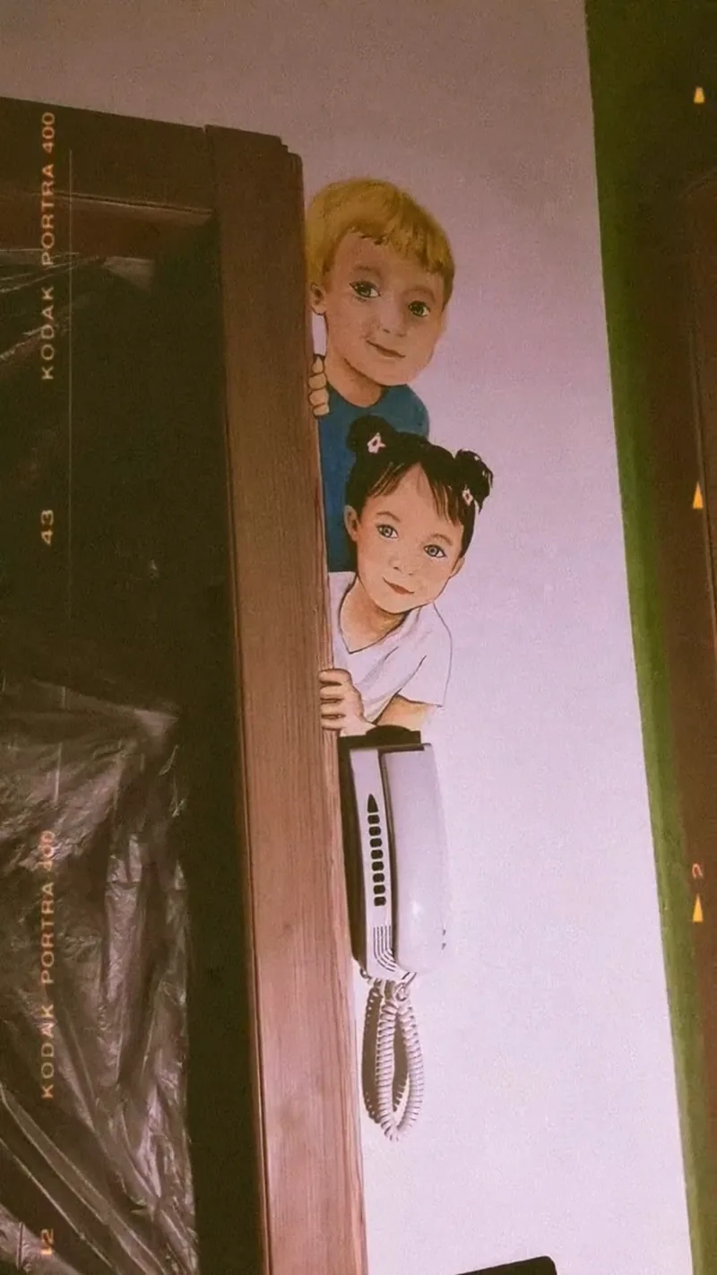 Sur le mur d’une entrée, Giulia Dal Bon a peint deux enfants qui passent la tête derrière l’encadrement de la porte.