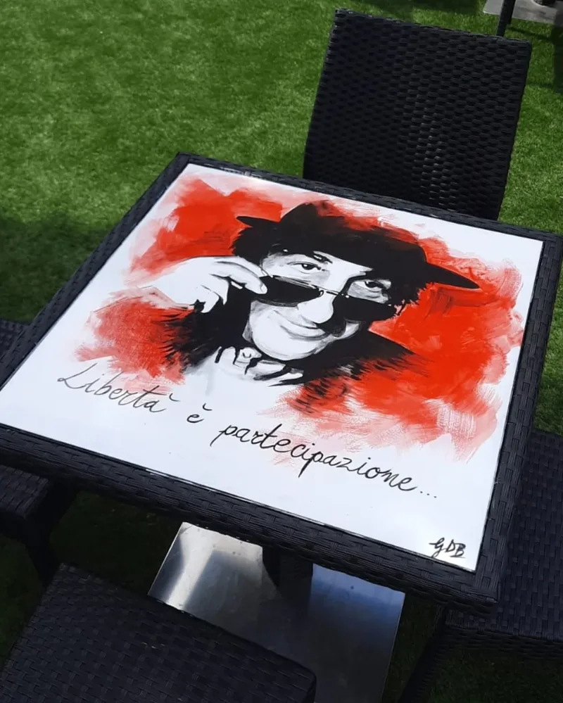 Sur le plateau d’une table, Giulia Dal Bon a peint le portrait d’un chanteur en noir sur un fond rouge, avec les mots d’une de ses chansons.