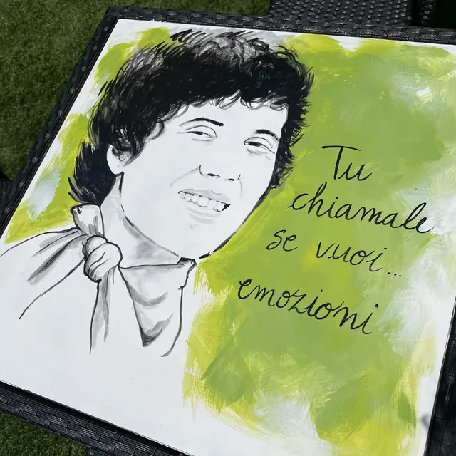 Giulia Dal Bon a peint un chanteur souriant sur un plateau de table, en noir sur un fond vert, et a écrit à la main les paroles d’une chanson.