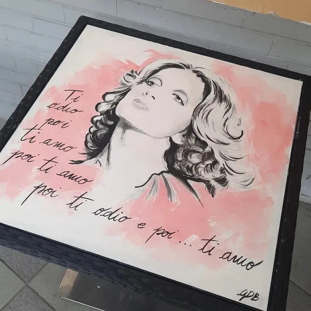 Giulia Dal Bon a peint une chanteuse en noir sur un fond rose, sur le plateau d’une table, entre les mots d’une de ses chansons.